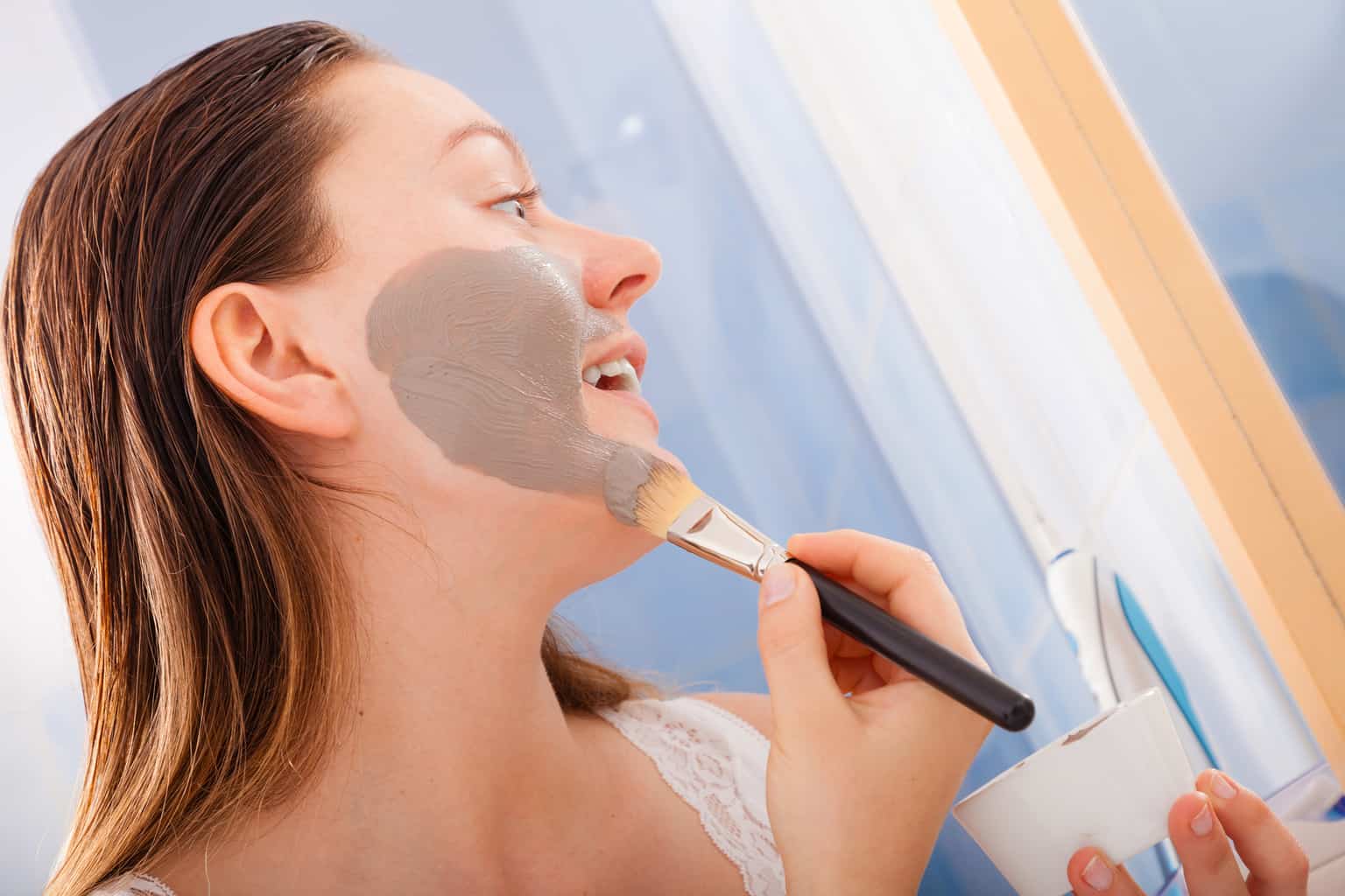 woman applying anti-aging mud face pack with brush