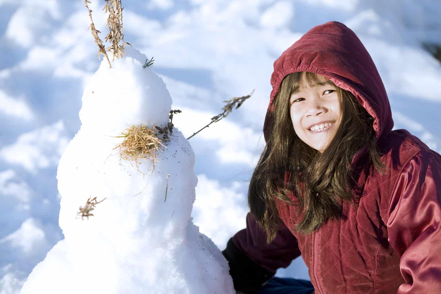 girl playing in the snow next to her little snowman, 12 days of christmas activity ideas for families
