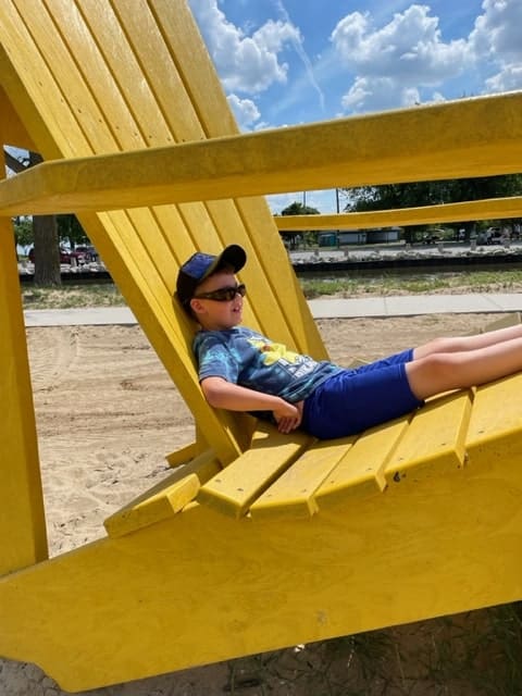 kid sitting in a giant yellow muskoka chair at the beach, fun cheap family activities summer weekends